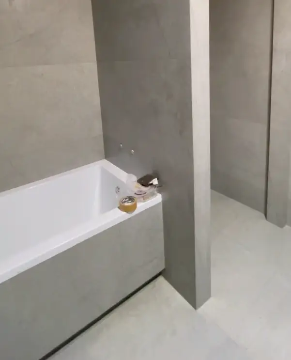 White alcove bathtub with large-format matte grey tiled apron and walls during a modern bathroom remodel.