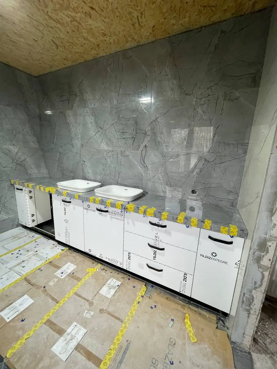 Unfinished modern bathroom vanity with white cabinets, a grey marble slab countertop, and three vessel sinks.
